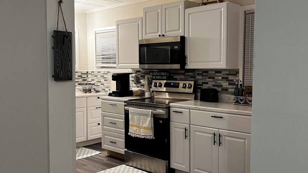 Una cocina moderna con armarios blancos, estufa de acero inoxidable y microondas.