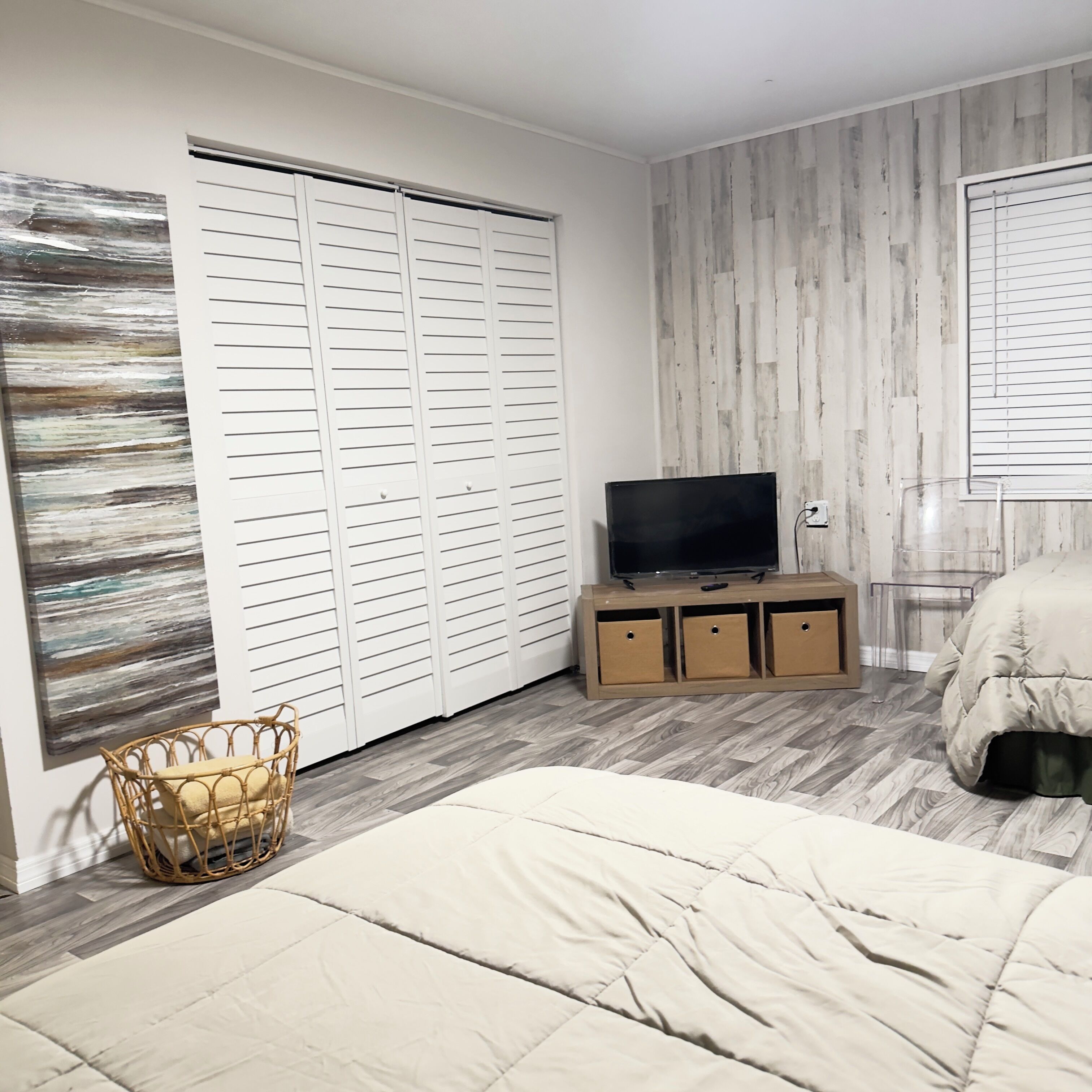 A bedroom with a bed, a TV on a wooden stand, a wardrobe, and a wall with a wooden panel design.