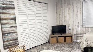 Un dormitorio con cama, televisor sobre un mueble de madera, armario y pared con diseño de paneles de madera.