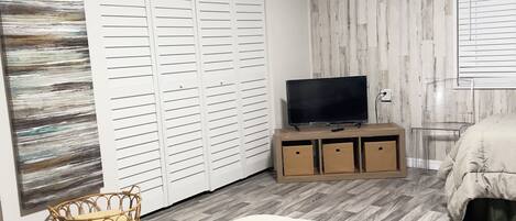 A bedroom with a bed, a TV on a wooden stand, a wardrobe, and a wall with a wooden panel design.