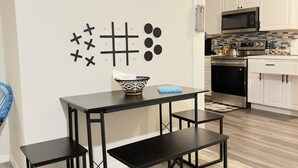 Una cocina moderna con armarios blancos, un microondas y una estufa. Hay una mesa negra con un tazón y un libro azul encima.