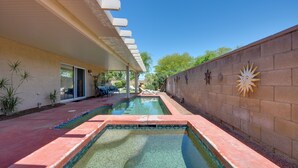 Una piscina con borde rojo, un patio cubierto y un muro de ladrillo con detalles decorativos.