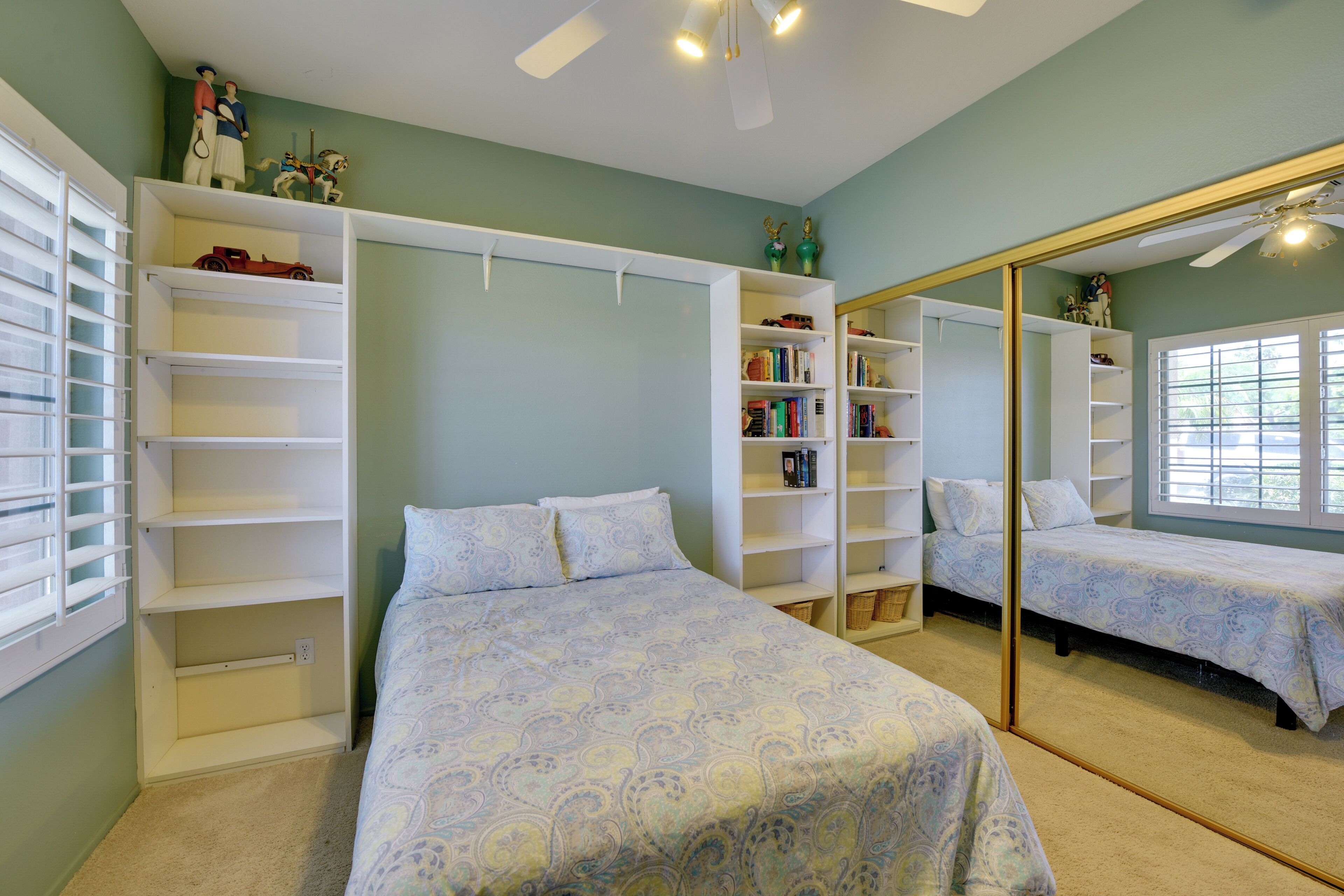 A bedroom with a bed, built-in shelving, a large mirror, and a ceiling fan.