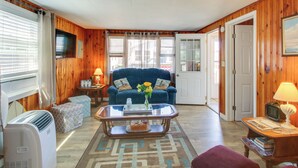 A living room with a blue sofa, a glass coffee table, and a television. - Cozy Hampton Cottage Near Marina & Nightlife (Hampton)