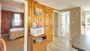 A room with wooden paneling, a bed, a microwave on a wooden cabinet, and a bathroom door. - Cozy Hampton Cottage Near Marina & Nightlife (Hampton)