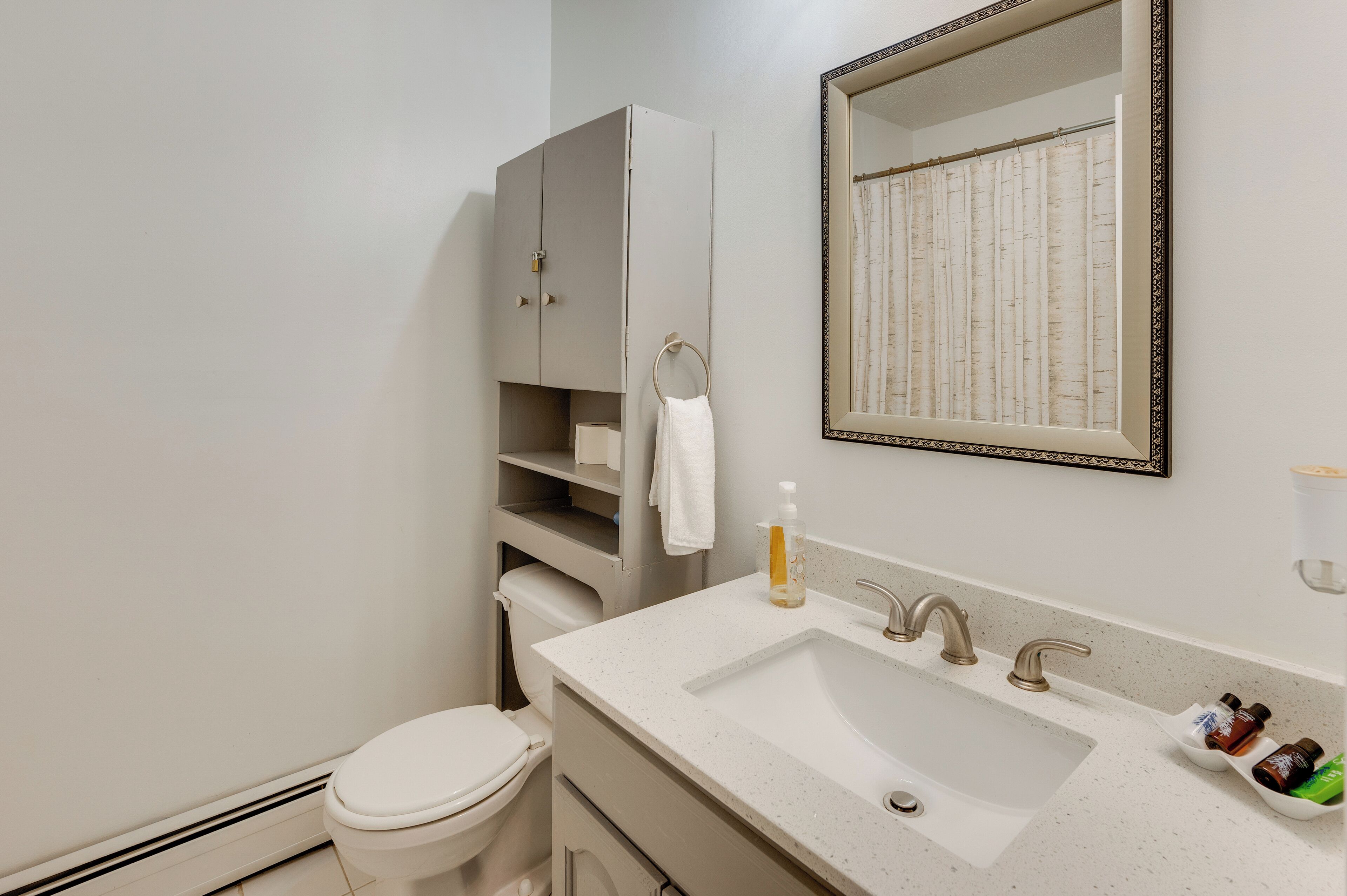 A bathroom with a toilet, a sink with three faucets, a mirror with a decorative frame, and a towel hanging on a rack.