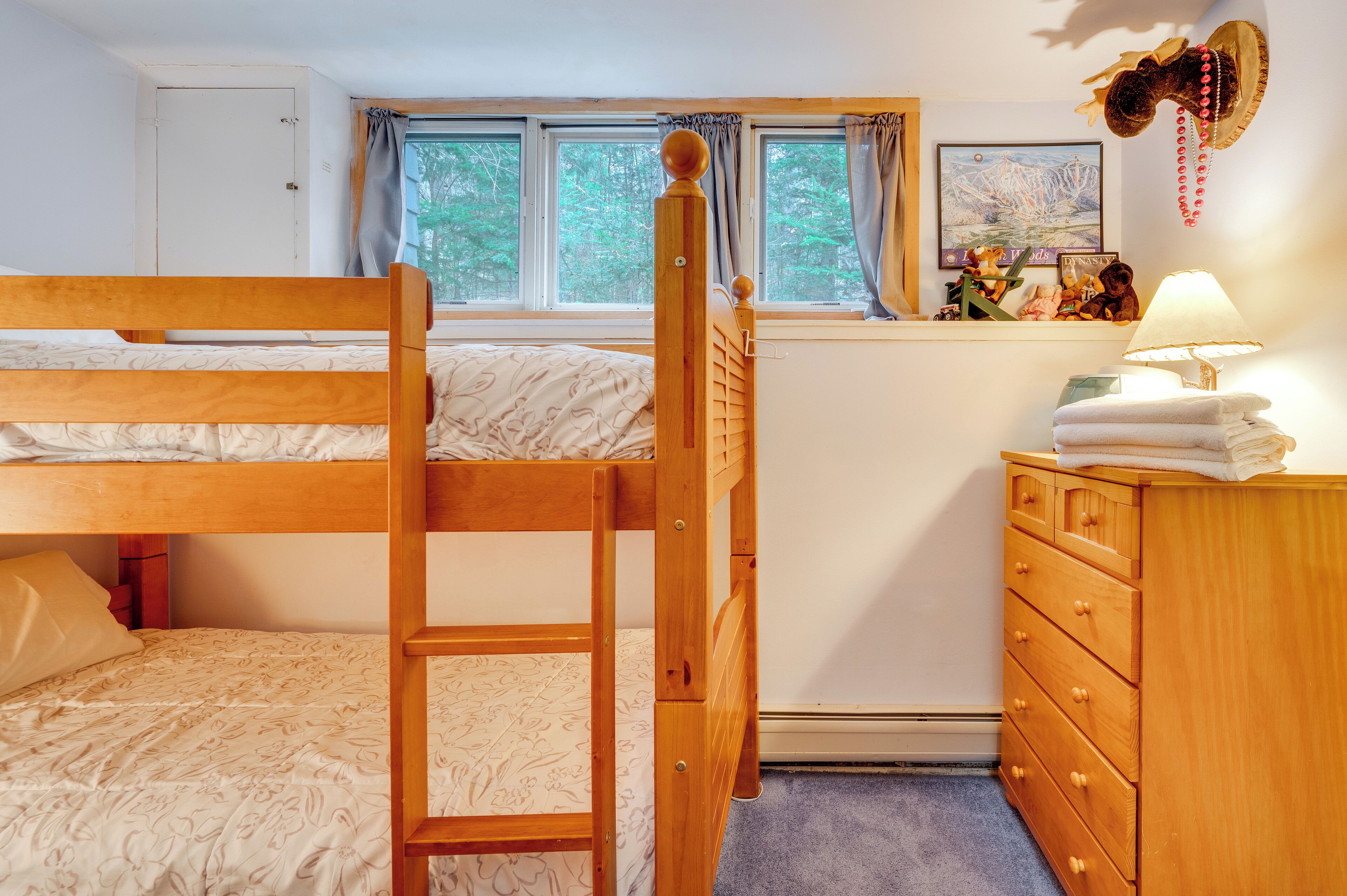 Habitación con literas, un aparador de madera y una ventana con cortinas.