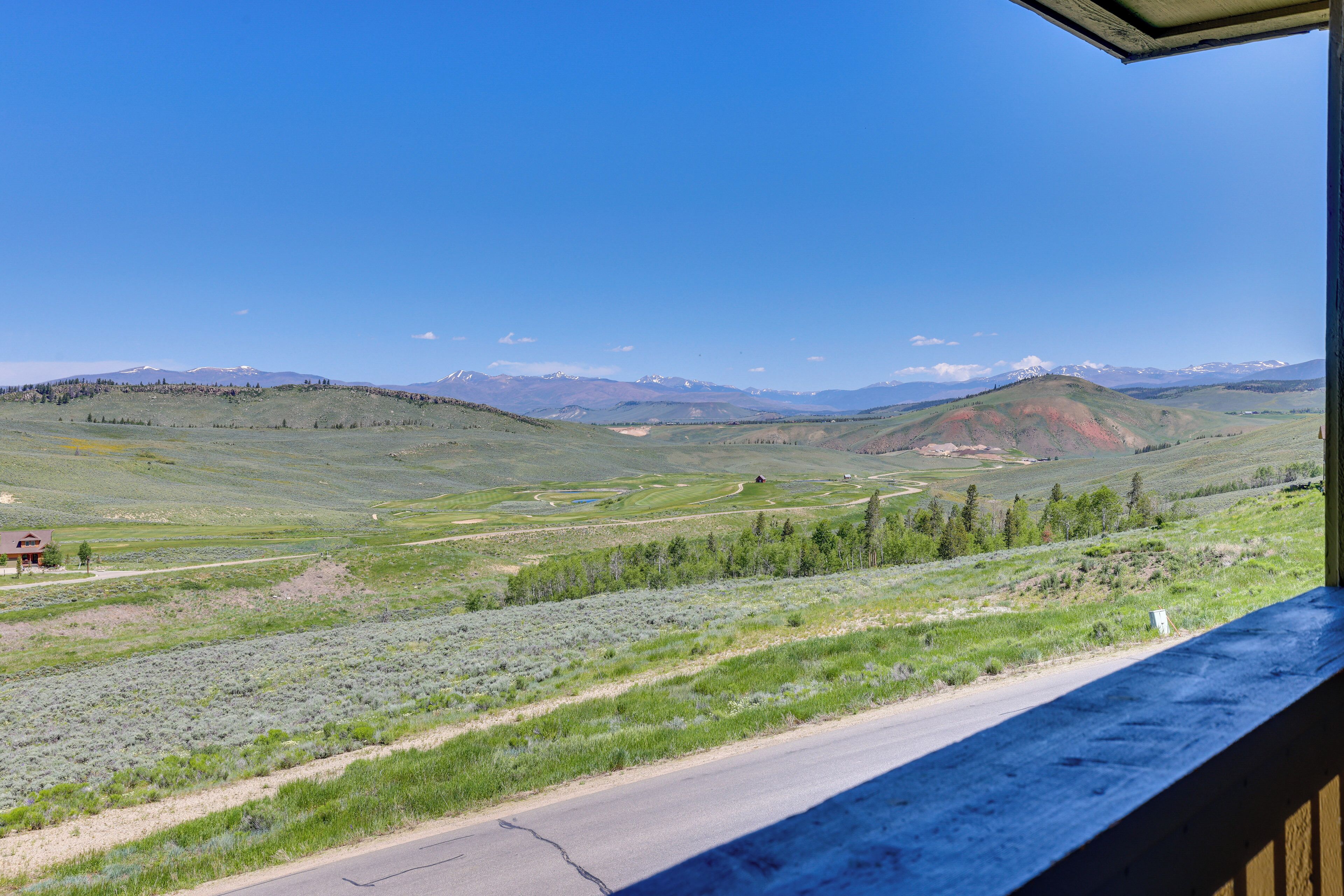 Une vue depuis un balcon donnant sur un paysage rural, avec des collines ondoyantes, une route et des montagnes au loin.