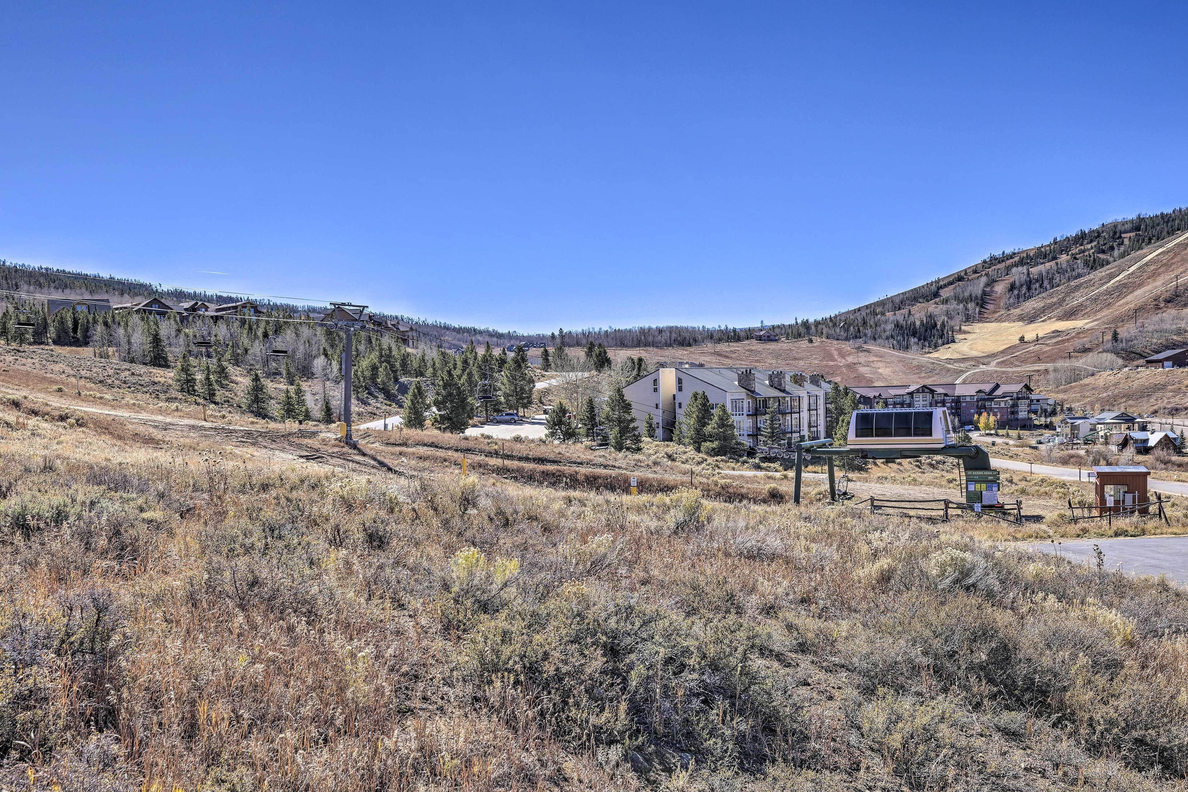 A rural area with a building that has a flat roof and a large window, surrounded by dry grass and trees.