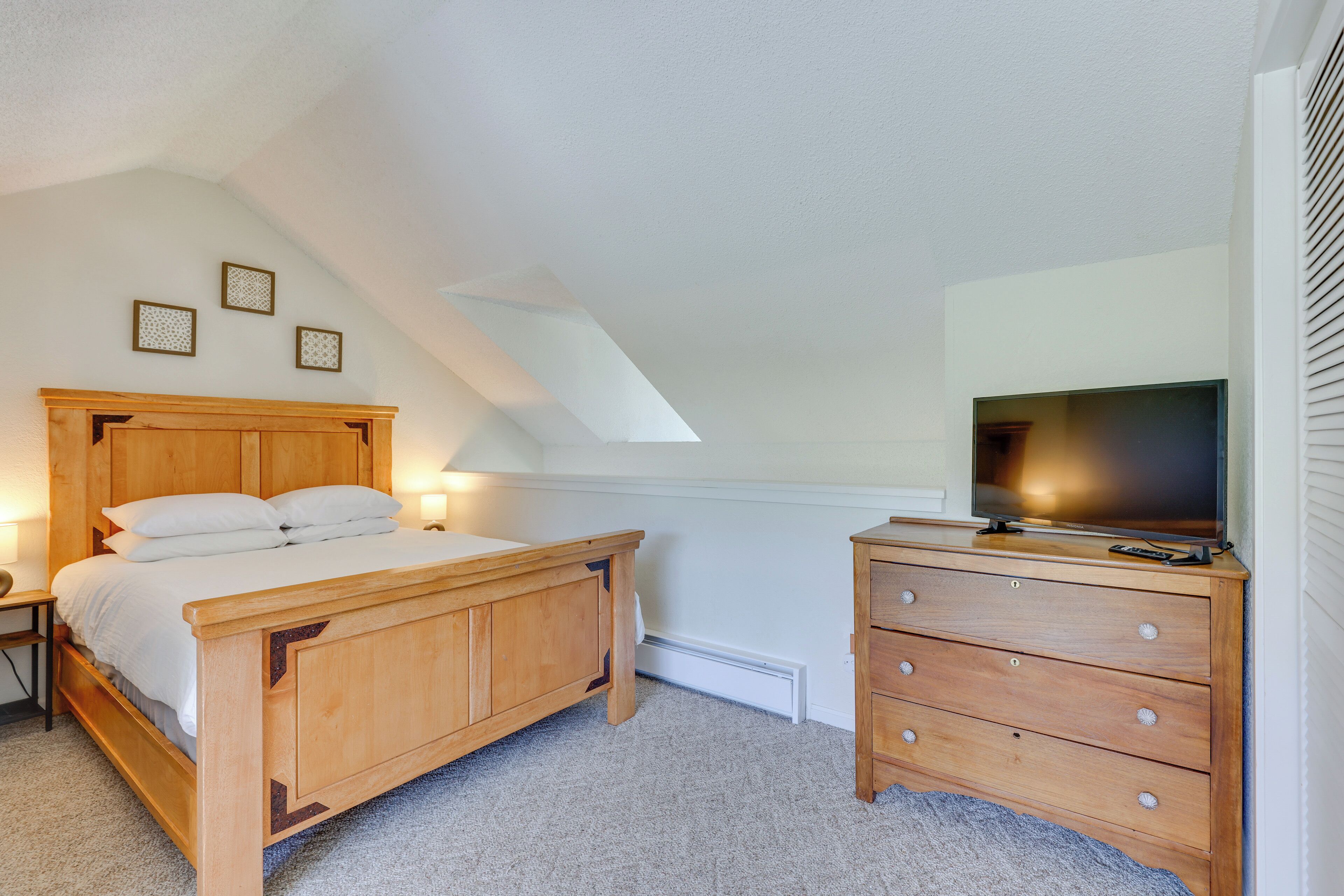 Ein Schlafzimmer mit einem hölzernen Bett, einem Schminktisch, einem Fernseher und drei gerahmten Bildern an der Wand.