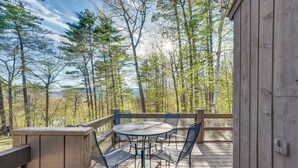 A wooden deck with a round table and chairs, surrounded by trees. - 0.5 Mi to Dtwn & Trails: Conway Condo w/ Hot Tub! (North Conway)
