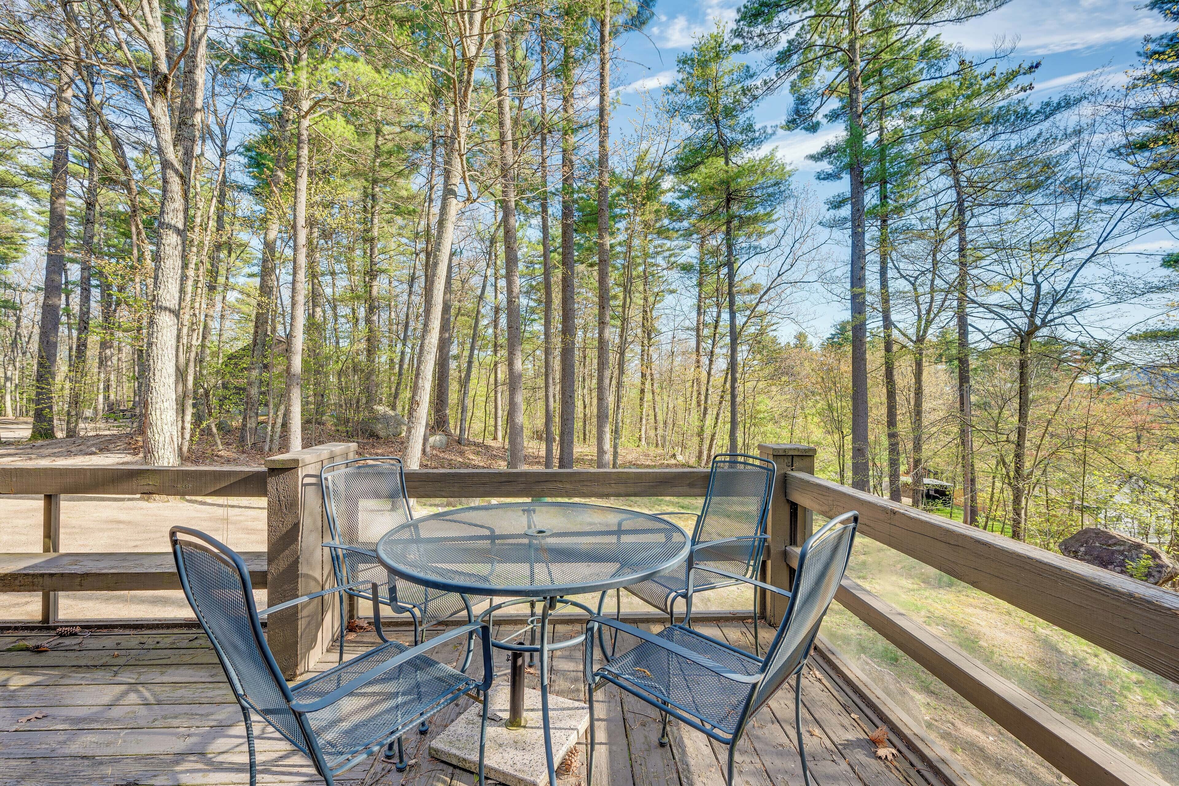 A wooden deck with a metal table and chairs, surrounded by tall trees.