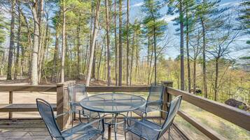 A wooden deck with a metal table and chairs, surrounded by tall trees.