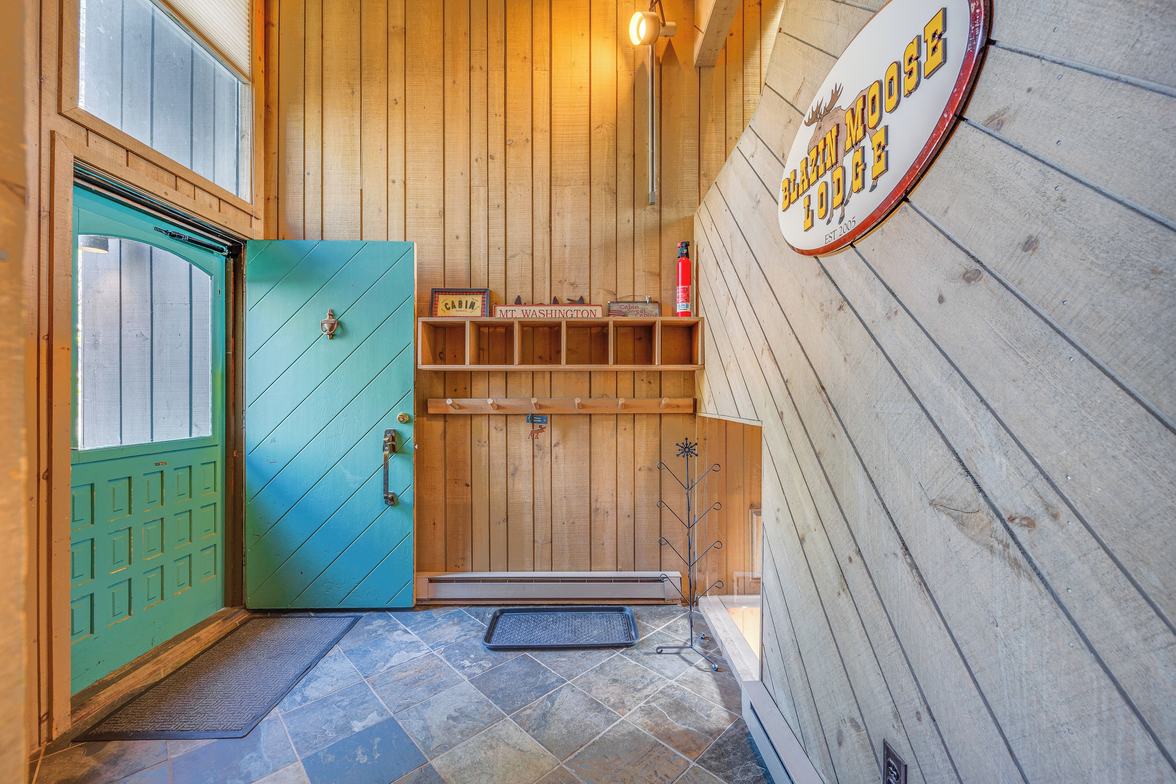 Een houten hut met een turquoise deur, een bord met daarop 'Mtn. Washington Moose Lodge' en een plank met een bordje en een brandblusser.