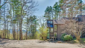 A modern house with a large driveway, surrounded by tall trees and a clear sky. - 0.5 Mi to Dtwn & Trails: Conway Condo w/ Hot Tub! (North Conway)