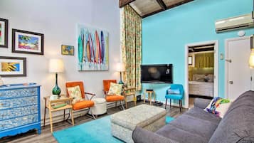 A living room with a sofa, chairs, a coffee table, a TV, and a painting of surfboards.
