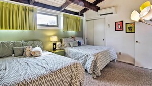 A bedroom with two beds, green curtains, a lamp, and wall art. - Walk to Dewey Beach: Bright Condo w/ Balcony! (Dewey Beach)