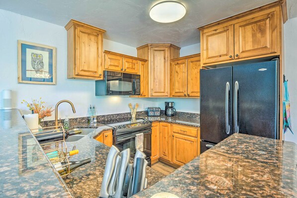 A kitchen with wooden cabinets, granite countertops, a stainless steel refrigerator, a microwave, and a stove.
