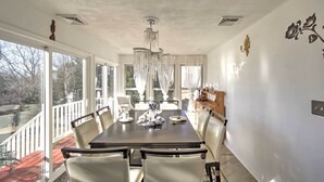A dining room with a large table, chairs, a chandelier, and a view through large windows.