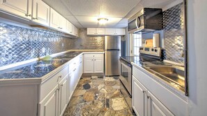 A modern kitchen with white cabinets, a stainless steel refrigerator, and a stone-patterned backsplash.