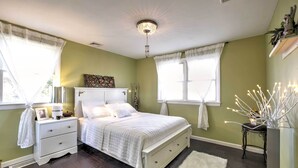 A bedroom with a bed, nightstands, a dresser, a chandelier, and a window with curtains.
