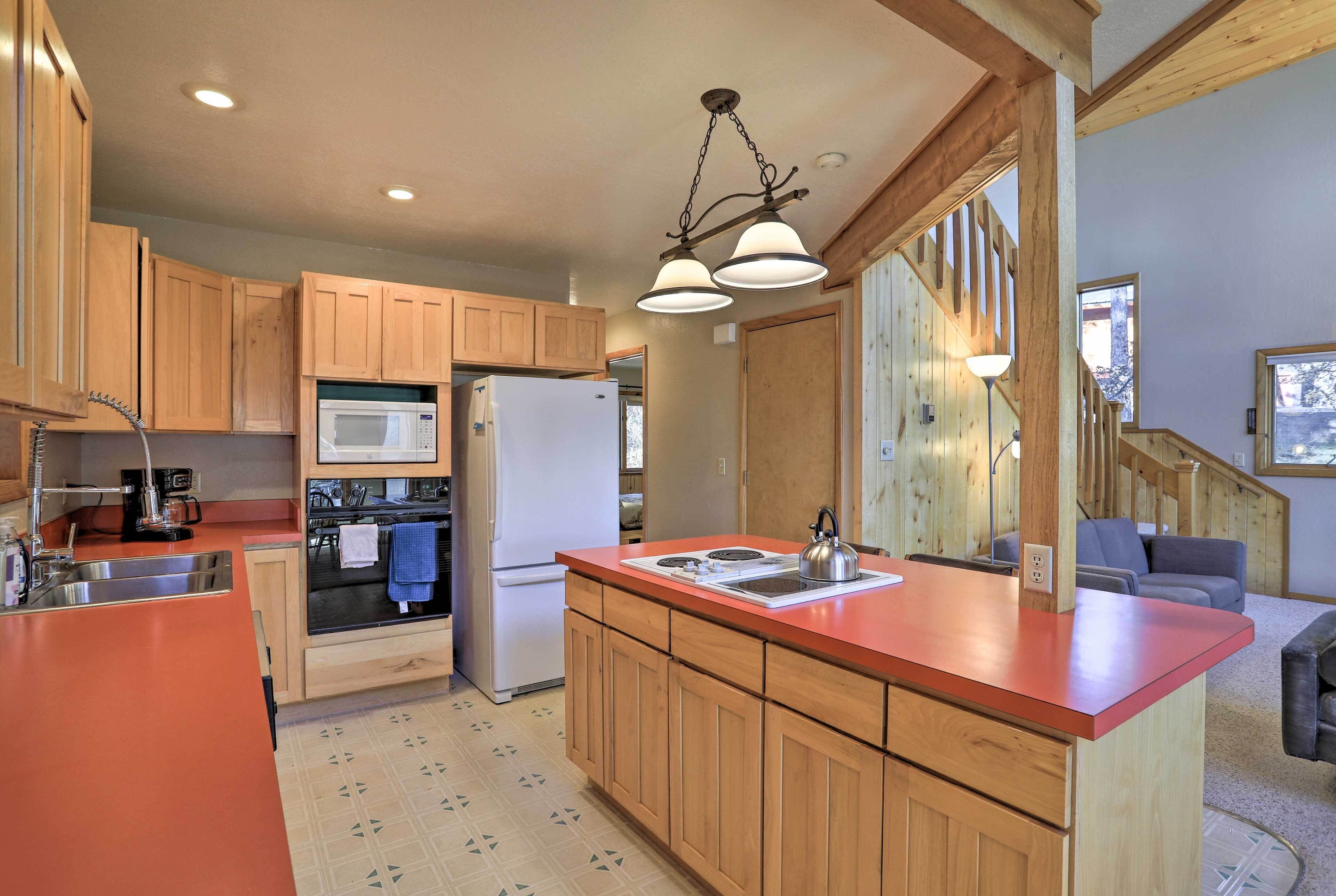 A kitchen with wooden cabinets, a red countertop, a microwave, a refrigerator, and a kettle.