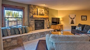 A cozy living room with a stone fireplace, a comfortable sofa, and a television. - Ski-in/out Access + Hot Tub! Breckenridge Condo (Breckenridge)