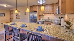 A kitchen with granite countertops, wooden cabinets, stainless steel appliances, pendant lighting, and a wine rack. - Ski-in/out Access + Hot Tub! Breckenridge Condo (Breckenridge)