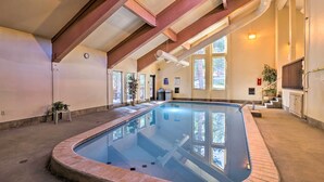 An indoor swimming pool with a brick border, large windows, and a high ceiling with exposed beams. - Ski-in/out Access + Hot Tub! Breckenridge Condo (Breckenridge)