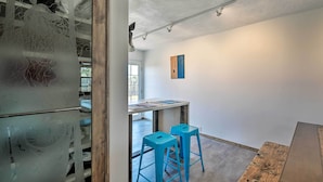 A modern interior with a glass partition, wooden bar counter, and two blue bar stools. - Chic Studio w/ Grill - 25 Mins to Taos Ski Valley! (El Prado)