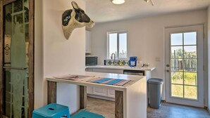 A modern kitchen with a central island, a decorative animal head, and a view through a glass door. - Chic Studio w/ Grill - 25 Mins to Taos Ski Valley! (El Prado)
