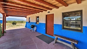A covered porch with a wooden ceiling, a blue and white exterior wall, a wooden door, and a window. - Chic Studio w/ Grill - 25 Mins to Taos Ski Valley! (El Prado)
