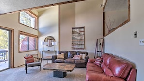 Ein geräumiges Wohnzimmer mit einer braunen Ledersitzgruppe, einem Holztisch und einem braunen Sofa. Ein großes Fenster lässt viel Tageslicht herein und bietet einen Blick ins Freie.