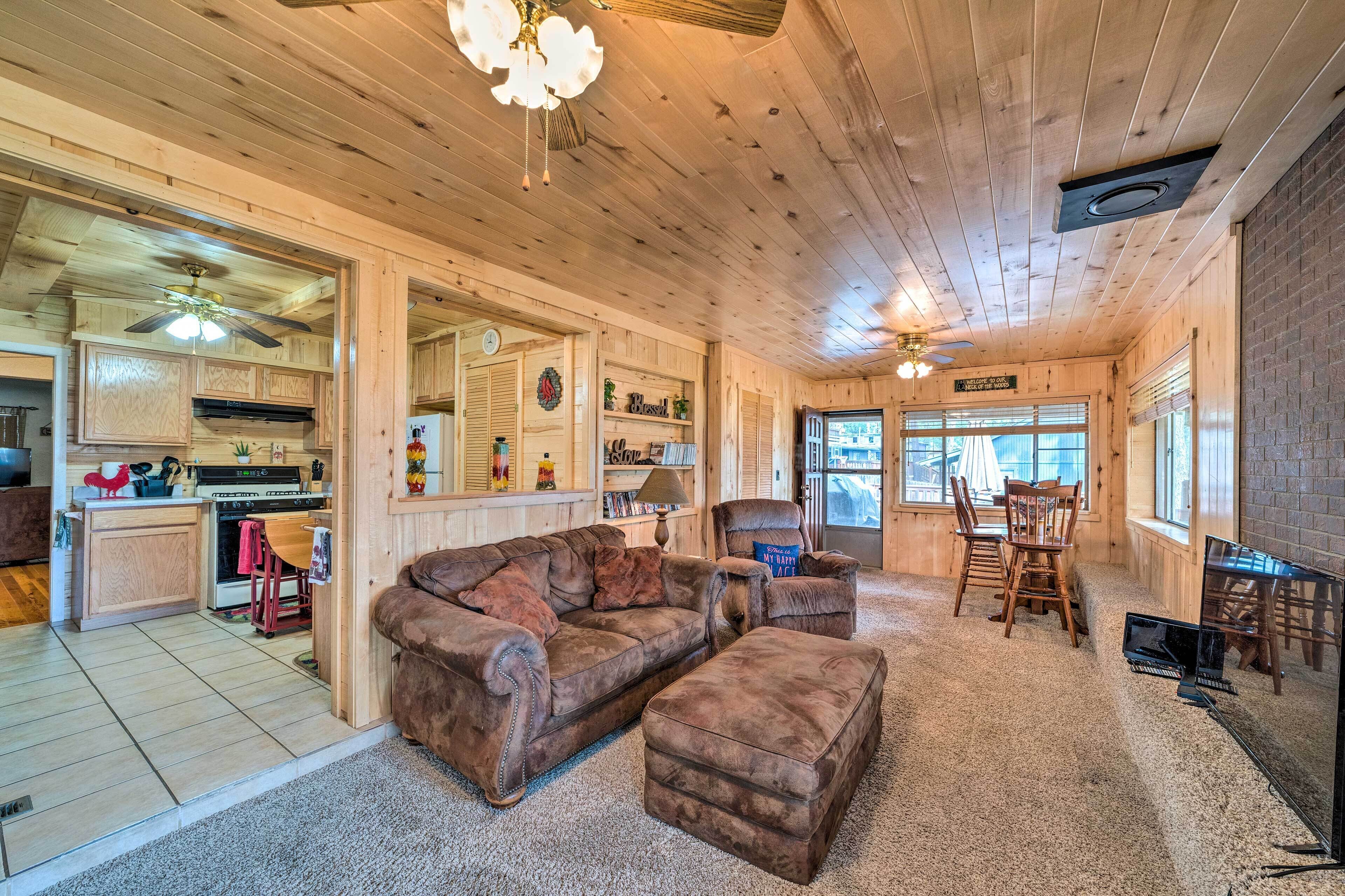 A cozy cabin interior with a wooden floor, a leather sofa, a dining table with chairs, and a kitchen area with a stove and cabinets.