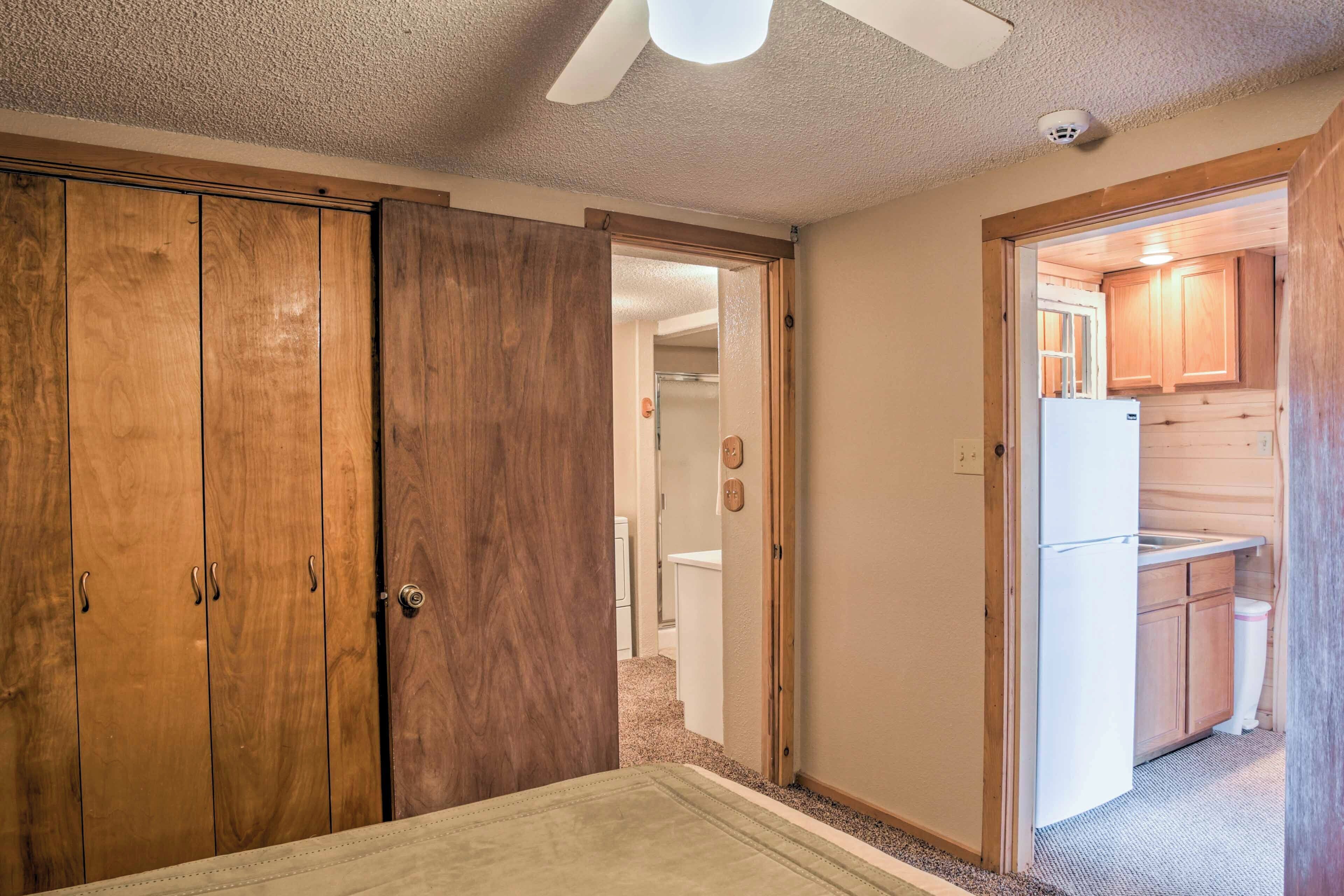 A room with wooden cabinets, a bed, and a kitchenette with wooden cabinets and a refrigerator.