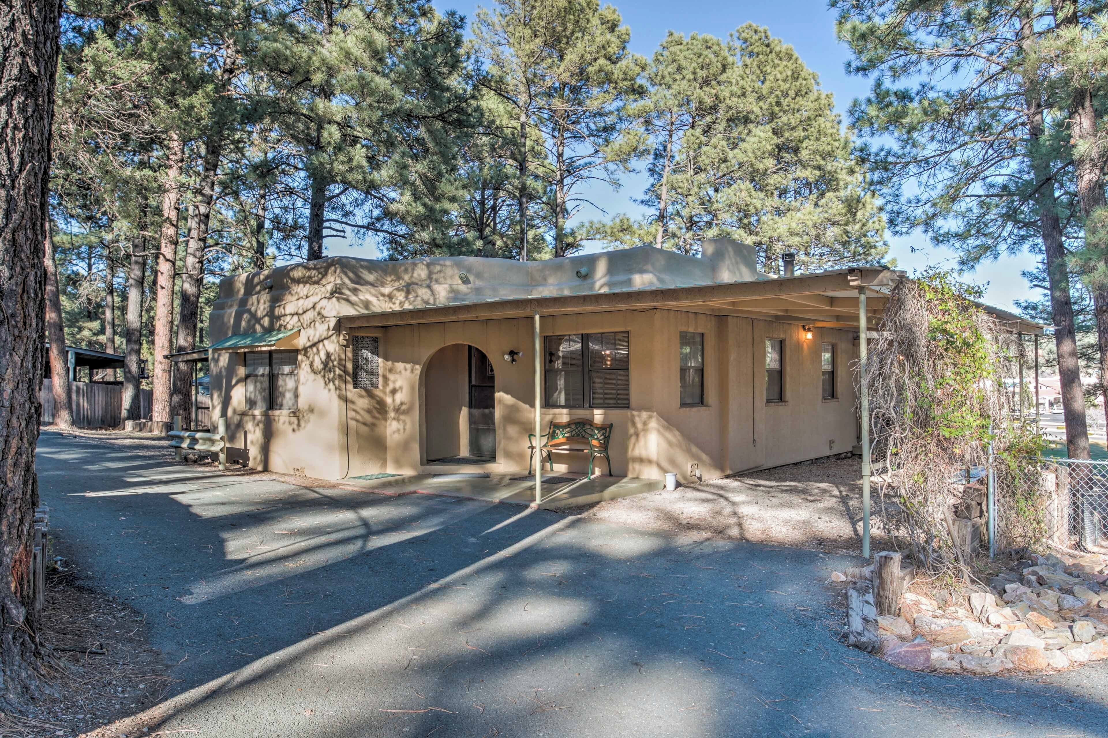 A single-story cabin with a covered porch, surrounded by tall pine trees.