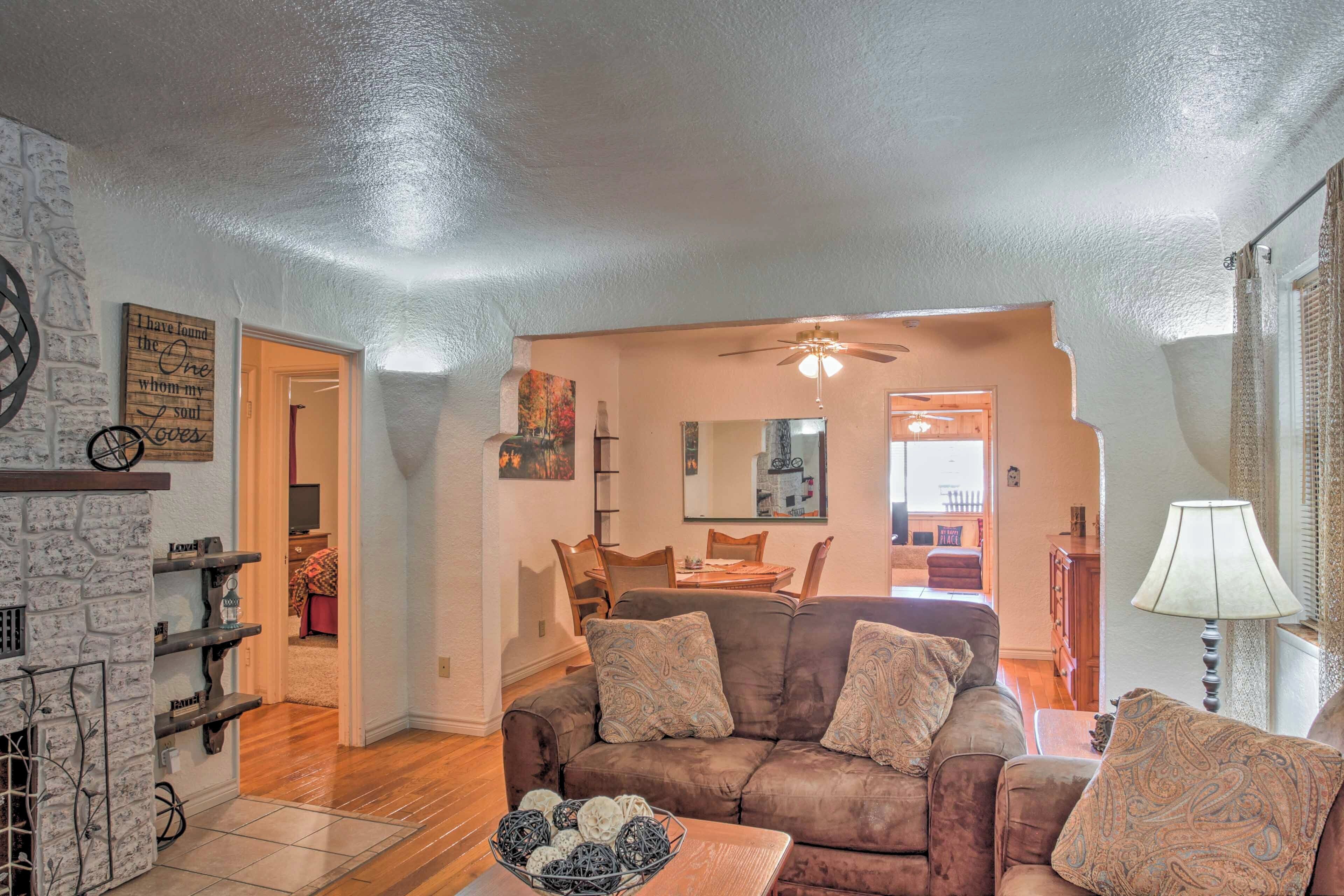 A cozy living room with a brown sofa, a coffee table with decorative items, a fireplace, and a dining area in the background.
