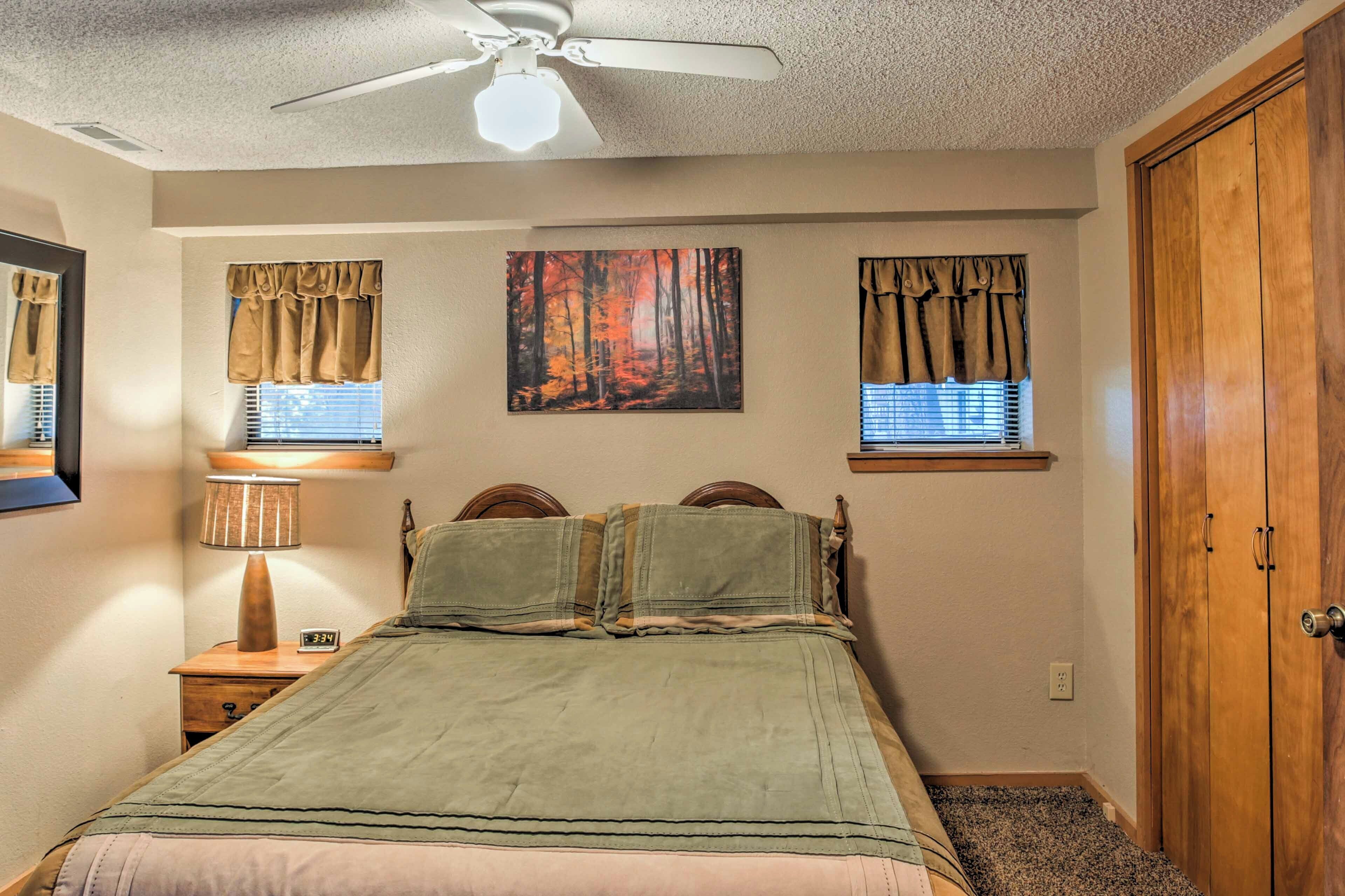 A bedroom with a bed, a ceiling fan, a nightstand with a lamp, and a wooden wardrobe.