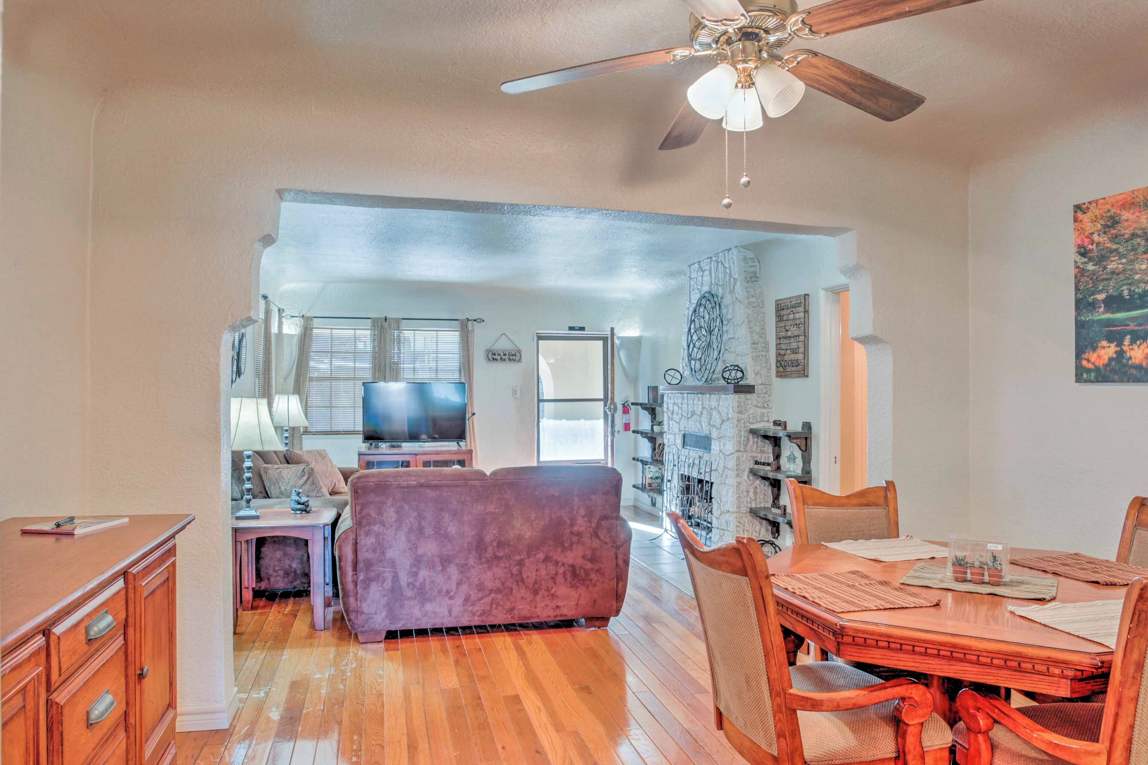 A spacious living room with a wooden floor, a purple sofa, a dining table with chairs, a ceiling fan, and a fireplace.