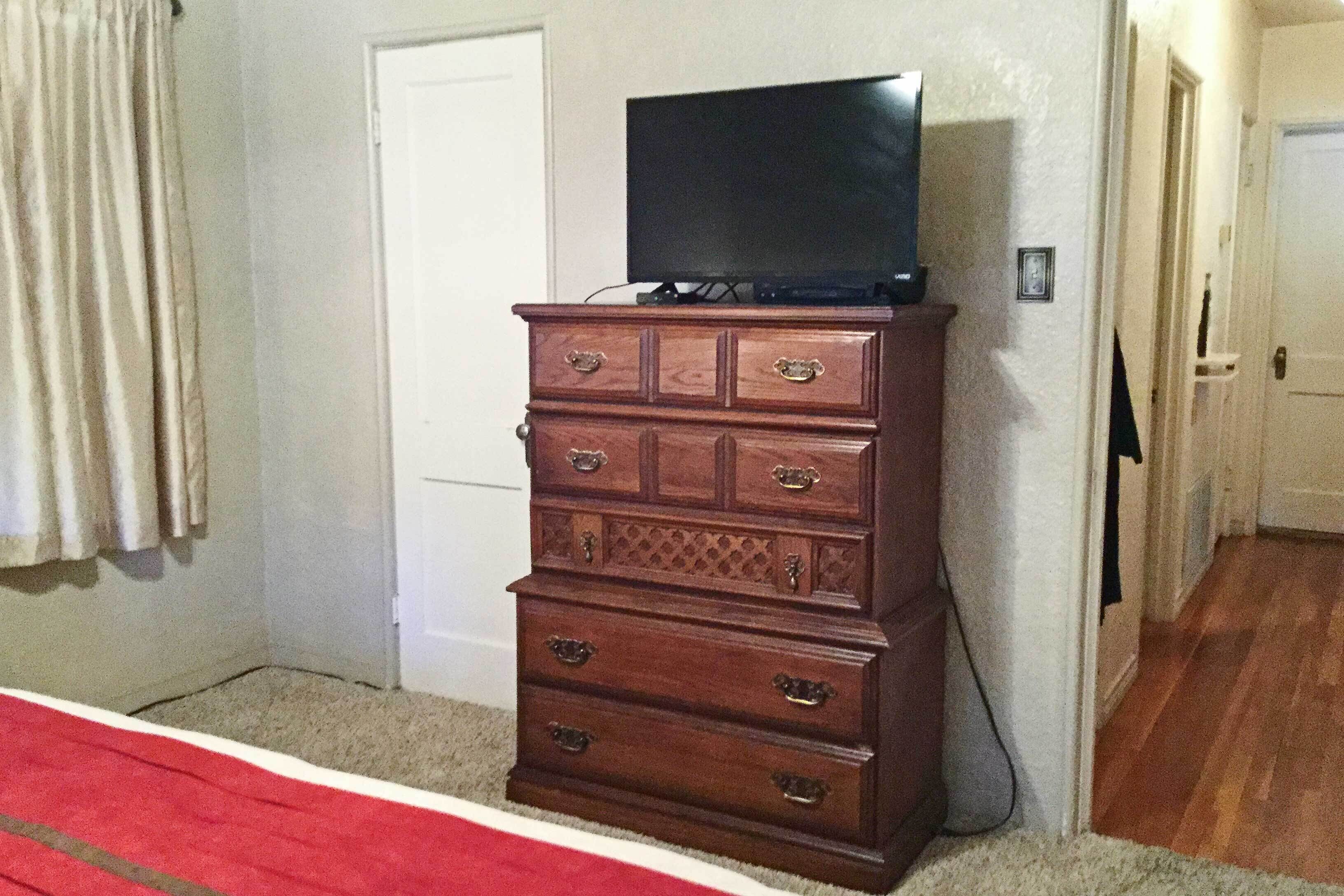 A wooden dresser with a television on top, a red carpet, and a white door in the background.