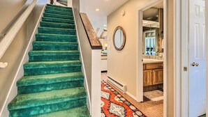 Un escalier recouvert d’une moquette verte mène à une pièce dotée d’un miroir et d’un sol carrelé.