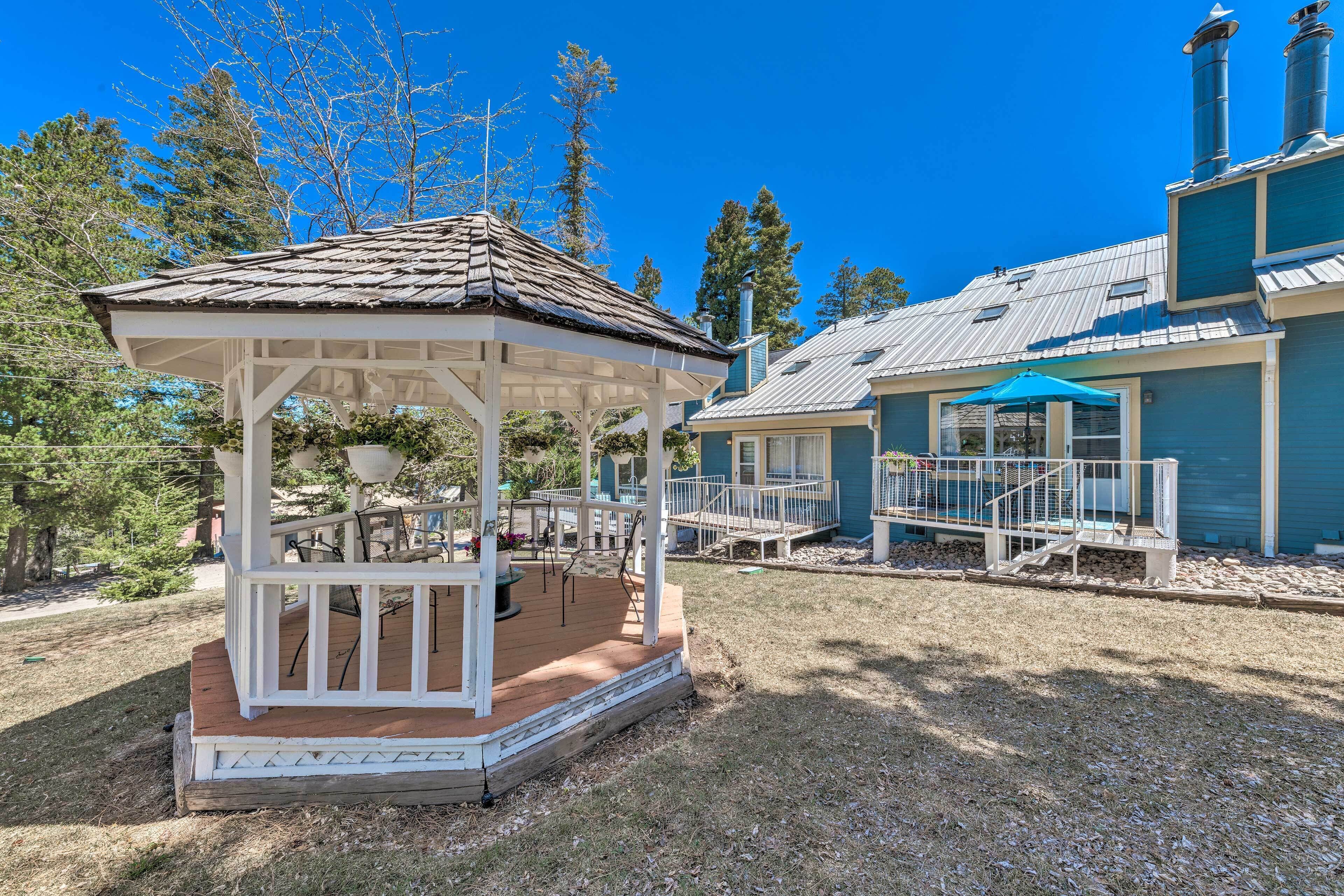 A gazebo with a wooden deck, a covered patio, and a building with a blue exterior and metal roof.