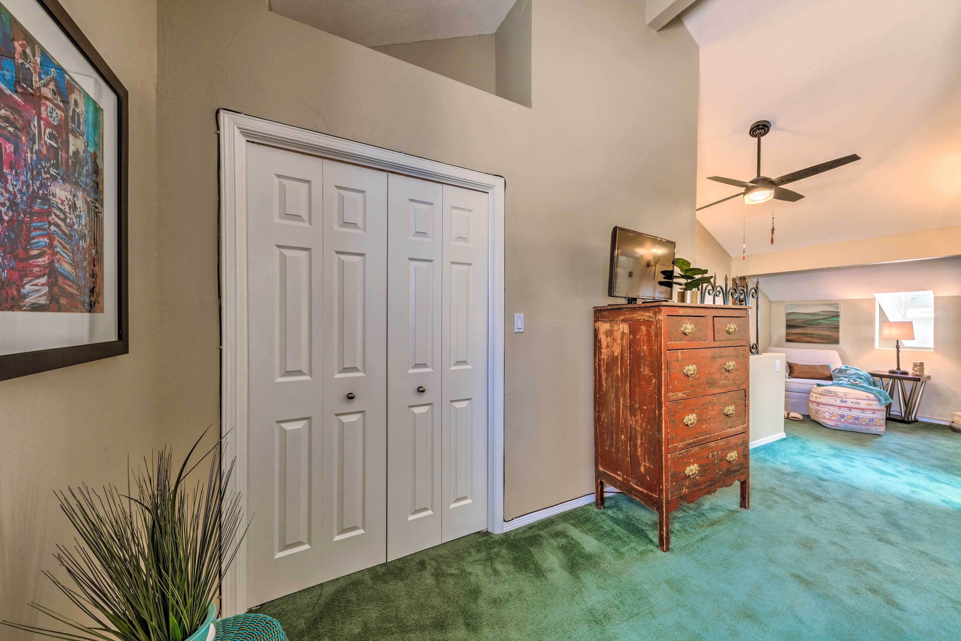 A hallway with a white door, a wooden dresser, a ceiling fan, and a painting on the wall.