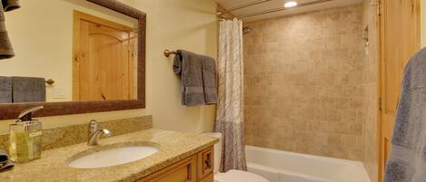 A bathroom with a sink, mirror, toilet, and bathtub.