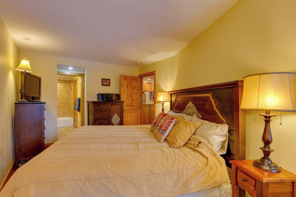 A bedroom with a large bed, wooden headboard, bedside table with a lamp, and a wooden wardrobe.