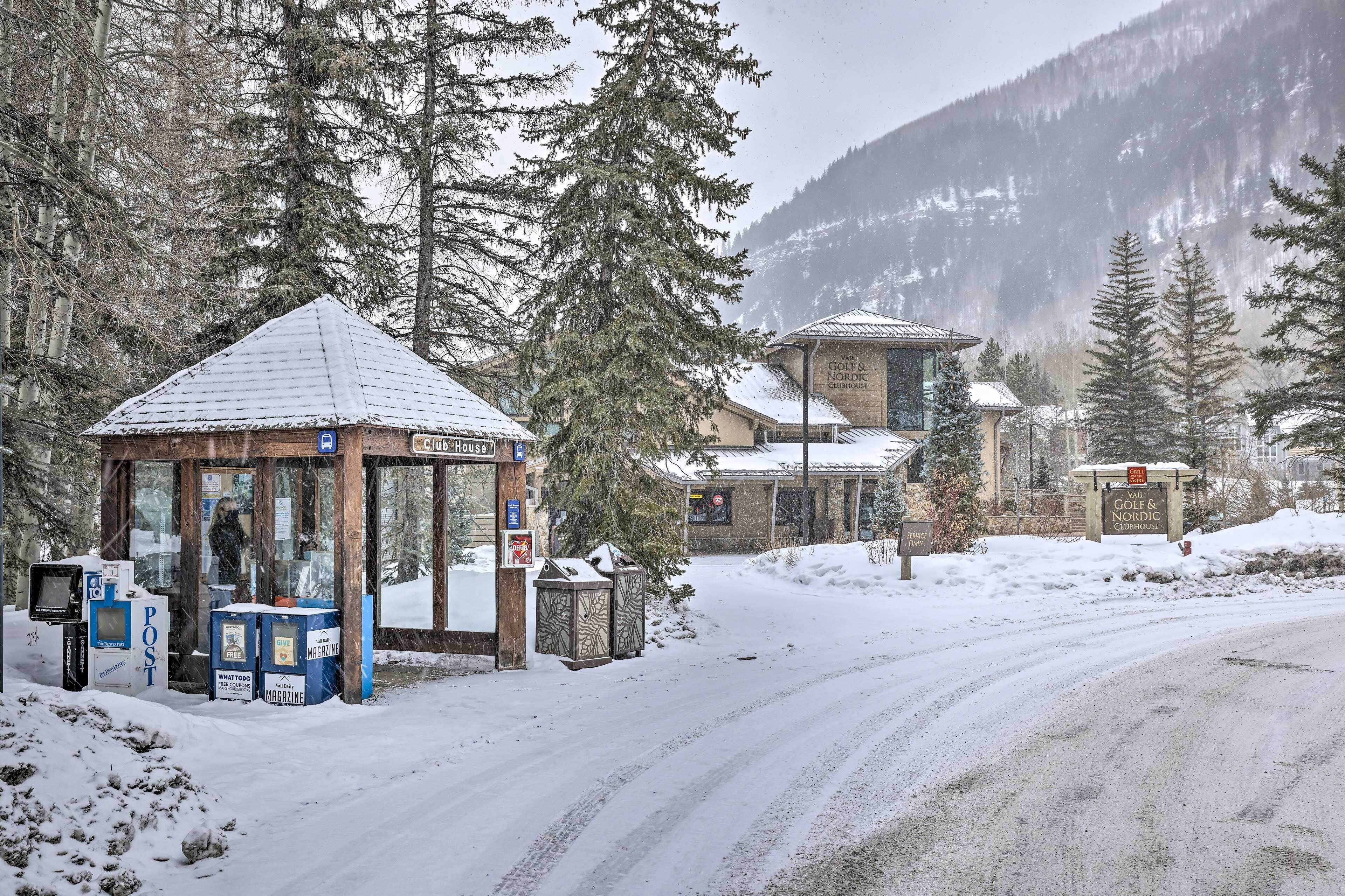 A snow-covered outdoor area with a wooden structure, possibly a kiosk or information booth, and a building in the background.