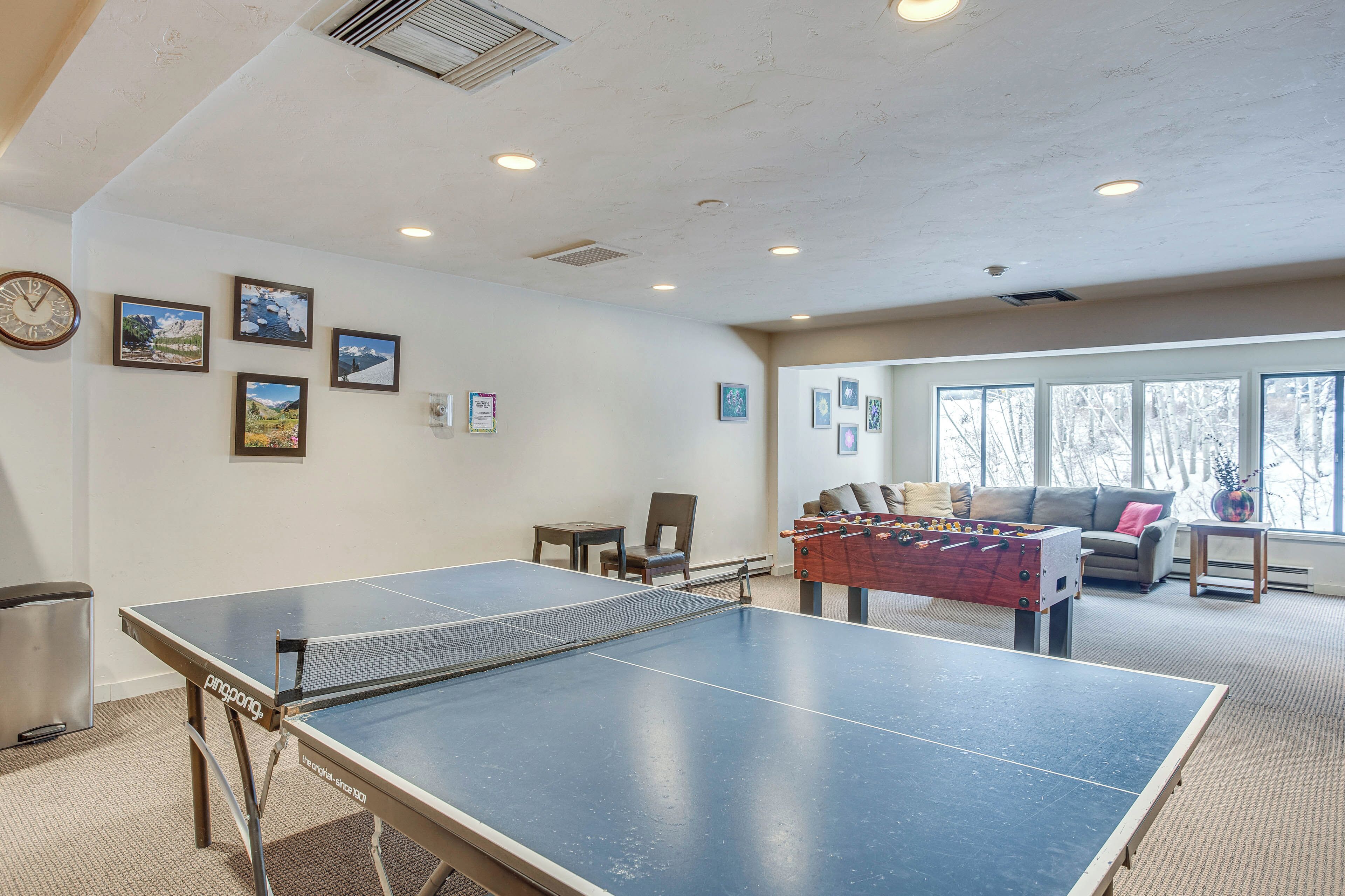 Una mesa de ping pong, una mesa de fútbol de mesa y un sofá en una habitación con ventanas grandes y cuadros en la pared.