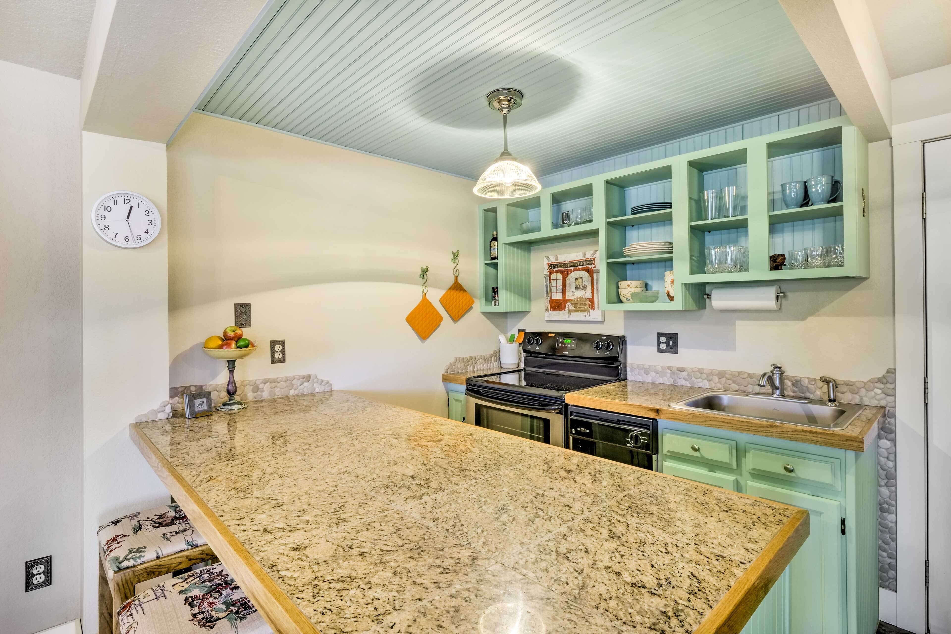 A kitchen with a granite countertop, green cabinets, a clock, and a hanging light fixture.
