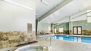 Une piscine intérieure dotée d’un jacuzzi, de murs carrelés et d’un espace détente avec des tables et des chaises.