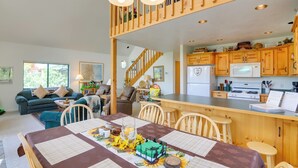 Amplia sala de estar con una mesa de comedor para cuatro, una cocina con armarios de madera y una escalera que lleva a un nivel superior.